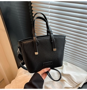 Close-up of black woven leather bucket bag with top handles and fashion logo plaque