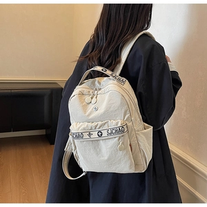 Rear view of a beige nylon backpack worn by a model, highlighting its compact size