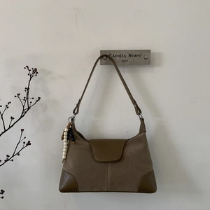 Detail of suede shoulder bag with leather trim and wooden bead charm on white wall