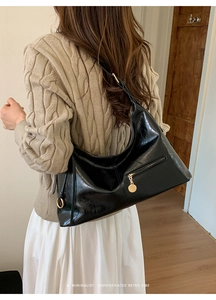 Detail of black crescent shoulder bag featuring glossy crinkled leather and gold hardware