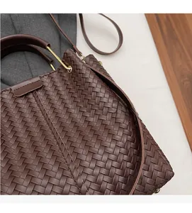 Detail of dark brown woven tote bag showing leather texture and gold metal handle joints