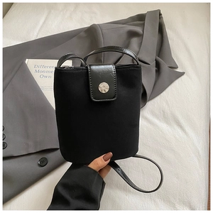 Detail of minimalist black crossbody bucket bag with glossy flap and silver magnetic clasp