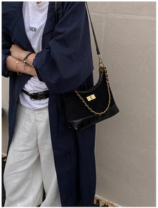 Detail of a black matte quilted shoulder bag with gold chain and turn-lock closure