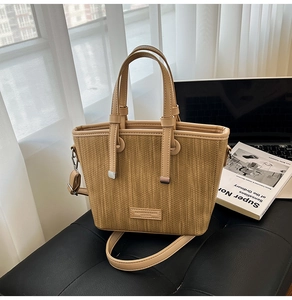 Detail of beige woven tote bag with adjustable strap and faux leather trim on black seat