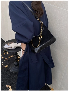 Detailed close-up of quilted suede hobo bag with golden chain strap in street style scene