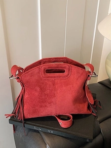 Red frosted suede handbag with fringe tassels and top handle on a minimalist background