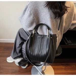 Close-up of black woven leather bucket bag with top handle and adjustable shoulder strap
