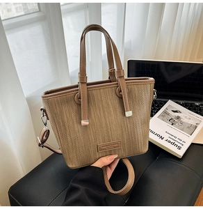 Close-up of brown woven bucket bag with leather handles and metallic rivet details