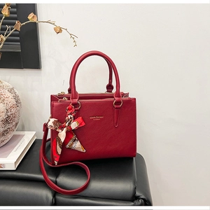 Detail of red lychee leather handbag with silk scarf and gold lettering in home setting