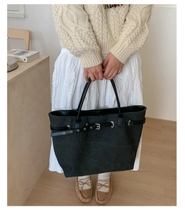 Detail of a large black canvas tote bag with slim leather straps held by a model