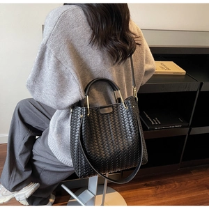 Detail of black woven leather tote bag featuring golden metallic handle accents