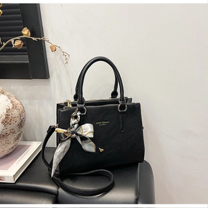 Detail of black pebbled leather handbag with silk scarf and adjustable strap