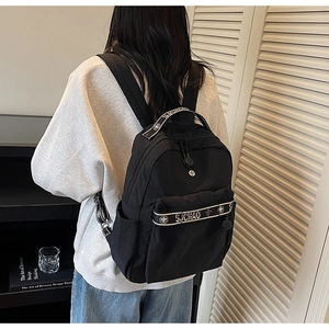 Detail of a minimalist black nylon backpack with lettered webbing on a female model