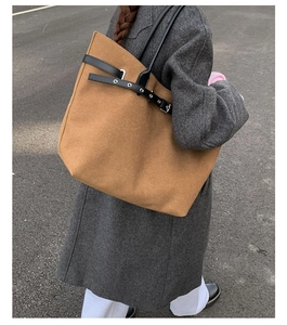 Close-up of a large brown canvas tote bag with black leather straps on a grey coat