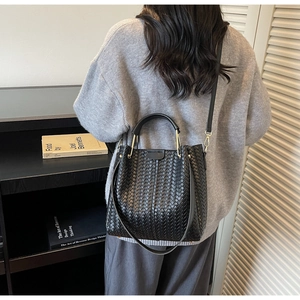 Detail of black woven leather bucket bag with gold hardware and long shoulder strap