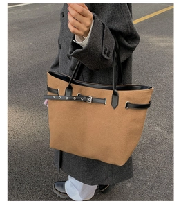 Outdoor street view of a large brown suede tote bag with black straps and metal eyelet details