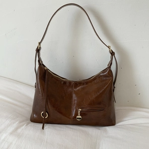 Close-up of dark brown glossy PU leather bag with wrinkled texture and gold hardware