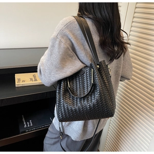 Detail of black woven bucket bag with elegant gold metal handles and textured finish