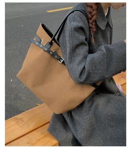 Detail of a brown canvas tote bag with black leather straps and metal eyelet accents