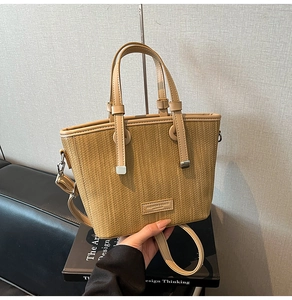 Detailed close-up of woven straw handbag featuring leather handles and brand plaque detail