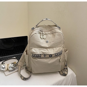 Detail of beige nylon backpack with SJ CHAO straps, laptop and headphones in office scene