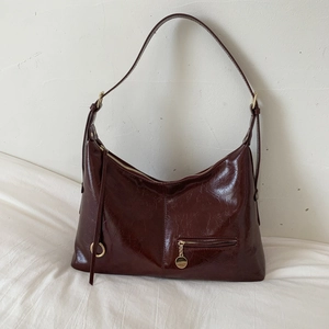 Detail of burgundy glossy oil wax leather hobo bag with vintage texture and metal zipper