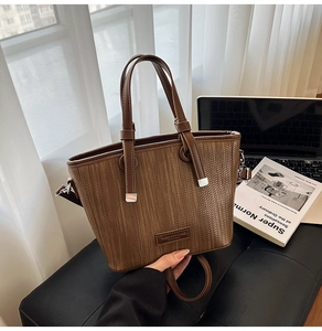 Detail of a brown woven leather tote bag with cylindrical handles and a shoulder strap