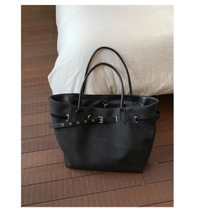 Detail of black canvas tote bag showing faux leather straps and silver buckle accents