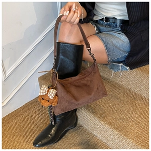 Détail d'un sac hobo en daim marron avec un pendentif ours en peluche sur la bandoulière