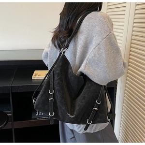 Detail of a black matte leather tote bag featuring multiple straps and silver metal buckles