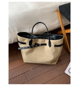 Detail of khaki canvas tote bag with black leather straps and shiny metal buckle