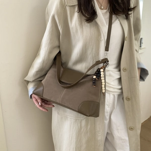 Close-up of brown suede shoulder bag with wood bead tassel and leather trim on beige coat