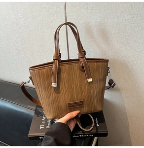 Detail of hand holding a dark brown woven tote bag with a leather fashion tag and strap