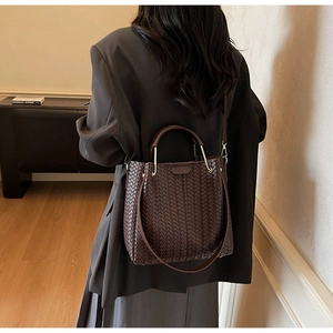 Detail of dark brown woven leather handbag with metal handle shown on shoulder