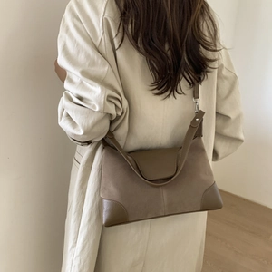 Detail view of brown suede and smooth leather拼接 shoulder bag worn by model in minimalist setting