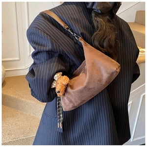 Détail du sac dumpling en daim marron avec un pendentif peluche teddy sur le côté