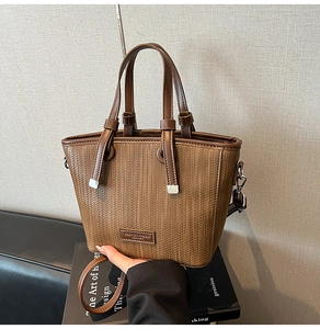 Macro detail of brown woven leather texture and logo tag on a stylish bucket handbag