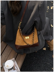 Detail of quilted suede crossbody bag with golden chain strap on autumn park bench