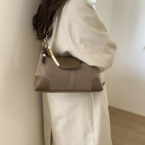 Brown suede shoulder bag with wood bead tassel shown on a beige trench coat model