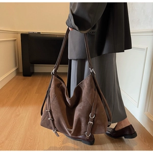 Detail of dark brown suede tote bag with adjustable metal buckle straps and matte texture