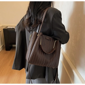 Detail of dark brown woven tote bag with metallic U-shaped handle and leather texture