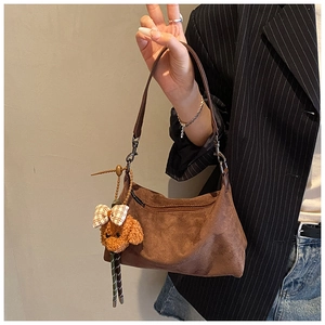 Détail d'un sac demi-lune en daim marron avec un pendentif ours mignon sur la bandoulière