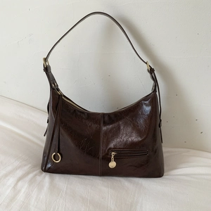 Detail view of dark brown high-gloss leather shoulder bag with golden pendant accent