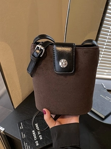 Deep brown suede bucket bag with black leather strap and round silver metal buckle