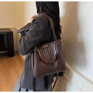 Detail of dark brown woven bucket bag featuring metal handles and adjustable strap