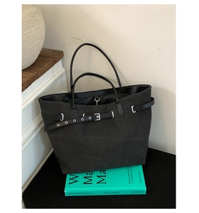 Detail view of black canvas tote bag with leather belt accents on a minimalist background