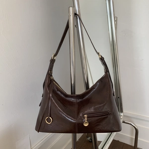 Detail of dark brown glossy leather dumpling bag with gold hardware and front zipper pocket