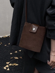 Minimalist brown suede bucket bag with round metal buckle worn by a model in autumn