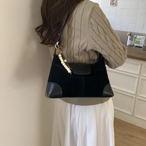 Detail view of black suede hobo bag with leather trim and beaded charm on model