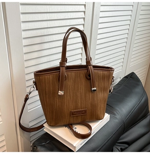 Detail of brown woven texture tote bag with metallic logo plate and adjustable strap